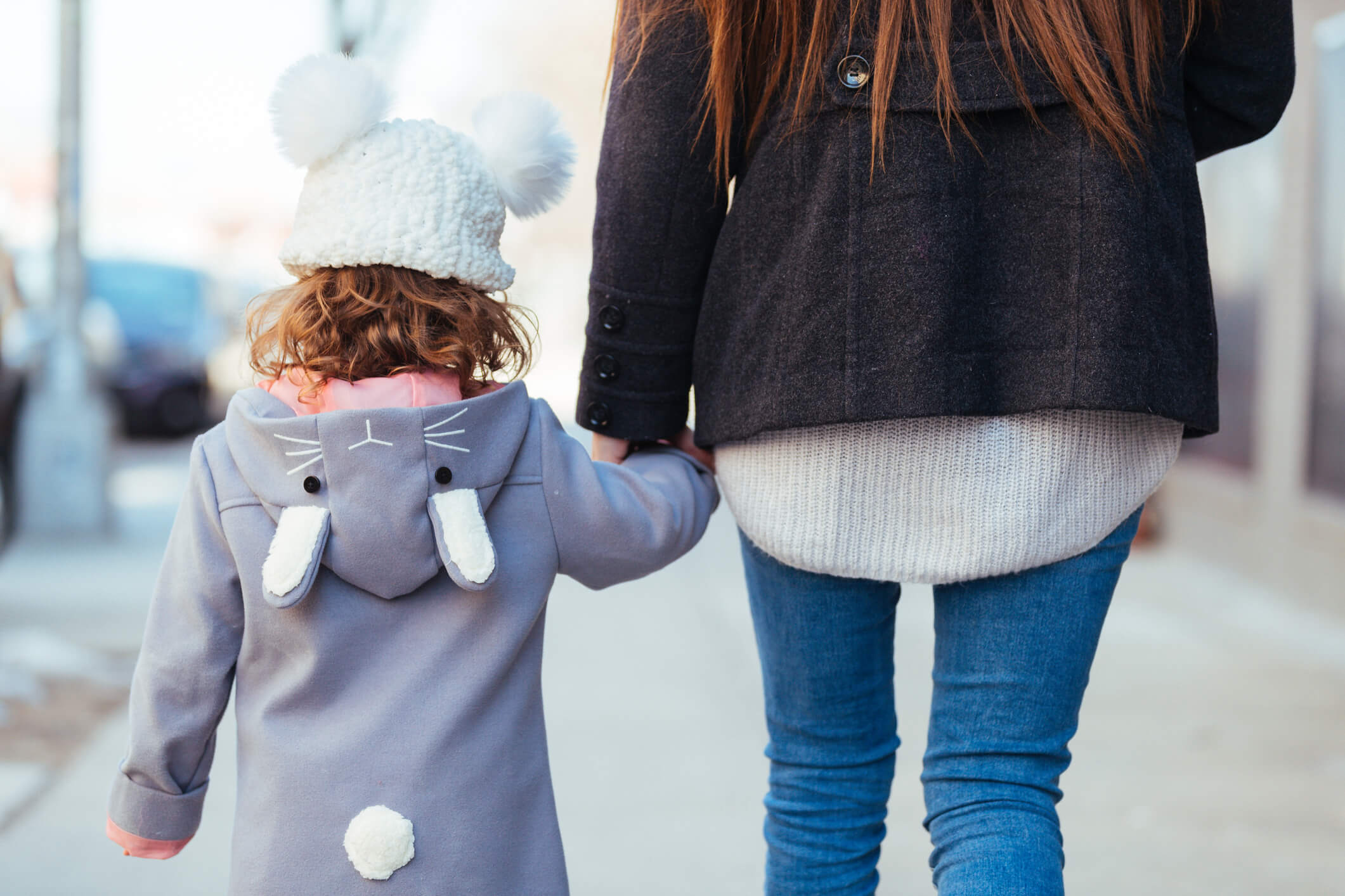 Daughter in winter coat and hat holding mom's hand